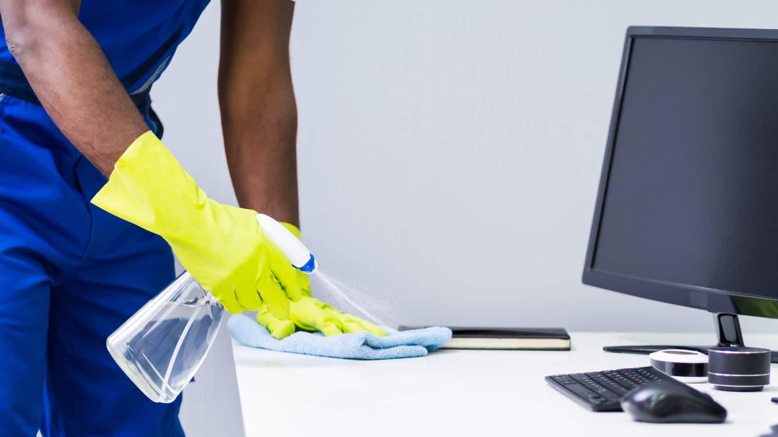 person with yellow gloves spraying cleaner on a desk