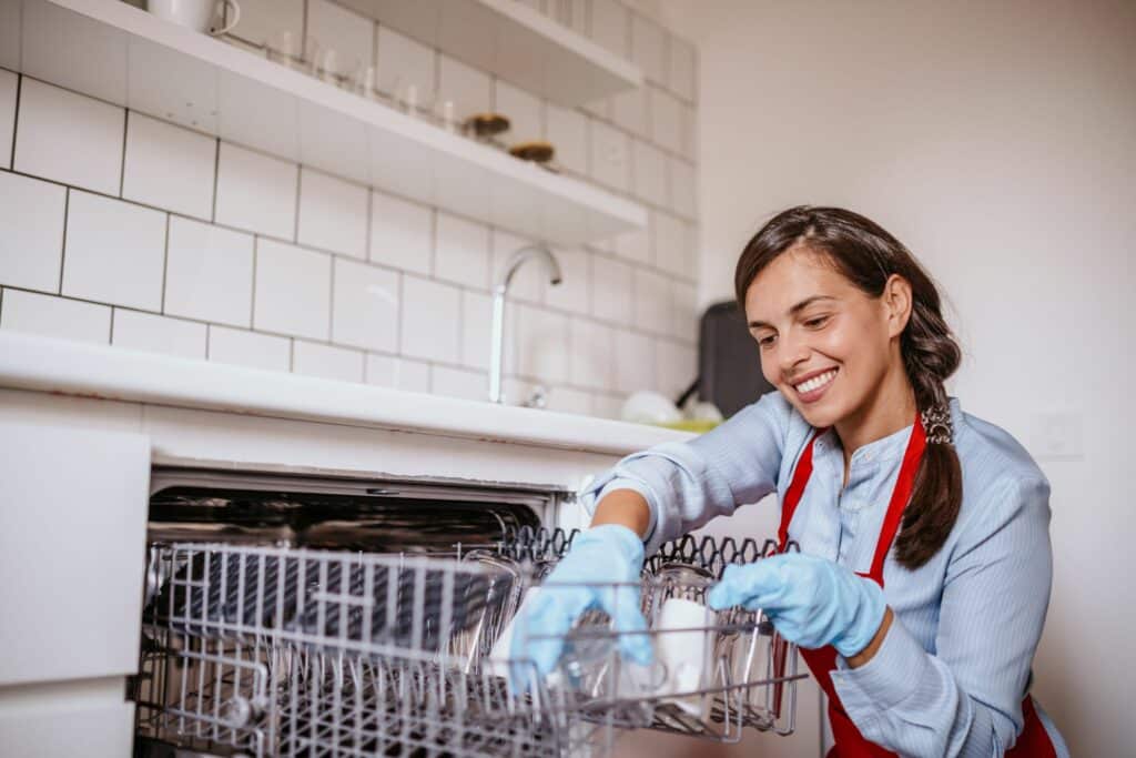 a woman in a long sleeve shirt and red apron undertaking the best way to clean a dishwasher